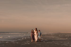 Moeder wandelt met haar twee kinderen hand in hand langs het strand tijdens zonsondergang in het Westland, ontspannen familieshoot moment.
