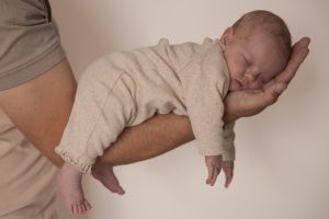 "Newborn fotoshoot met slapende baby in de hand van vader – pure en liefdevolle newbornfotografie in natuurlijke stijl"