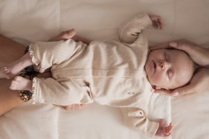 Newborn fotoshoot in natuurlijke stijl met slapende baby in beige pakje, vastgehouden door ouders, gefotografeerd door By Iris van der Zwan in ’s-Gravenzande, Westland, regio Den Haag.