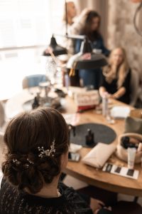 Vriendinnen tijdens de voorbereidingen van de bruiloft, een ontspannen moment aan tafel vastgelegd door By Iris van der Zwan, bruidsfotograaf in ’s-Gravenzande, Westland en regio Den Haag.