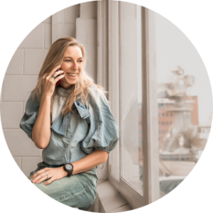 Professionele portretfoto van een lachende vrouw die telefoneert bij een groot raam, zachte beige en groene tinten, natuurlijk licht; moderne lifestylefotografie voor moeders en vrouwen in het Westland, ’s-Gravenzande en regio Den Haag door By Iris van der Zwan.