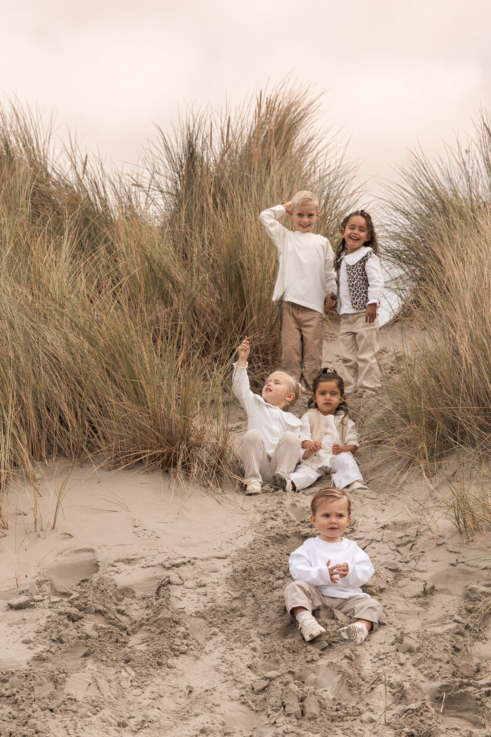 Liefdevolle lifestyle gezinsfoto op het strand, ouders wandelen met hun jonge kind in zachte beige tinten; warme en natuurlijke momentopname in de duinen, gefotografeerd door By Iris van der Zwan in het Westland, ’s-Gravenzande en regio Den Haag.