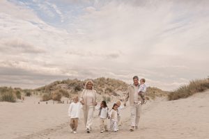 Lifestyle familiefoto op het strand met volwassen kinderen en ouders in zachte beige tinten; liefdevolle en spontane momentopname in de duinen, geportretteerd door By Iris van der Zwan in het Westland, ’s-Gravenzande en regio Den Haag.