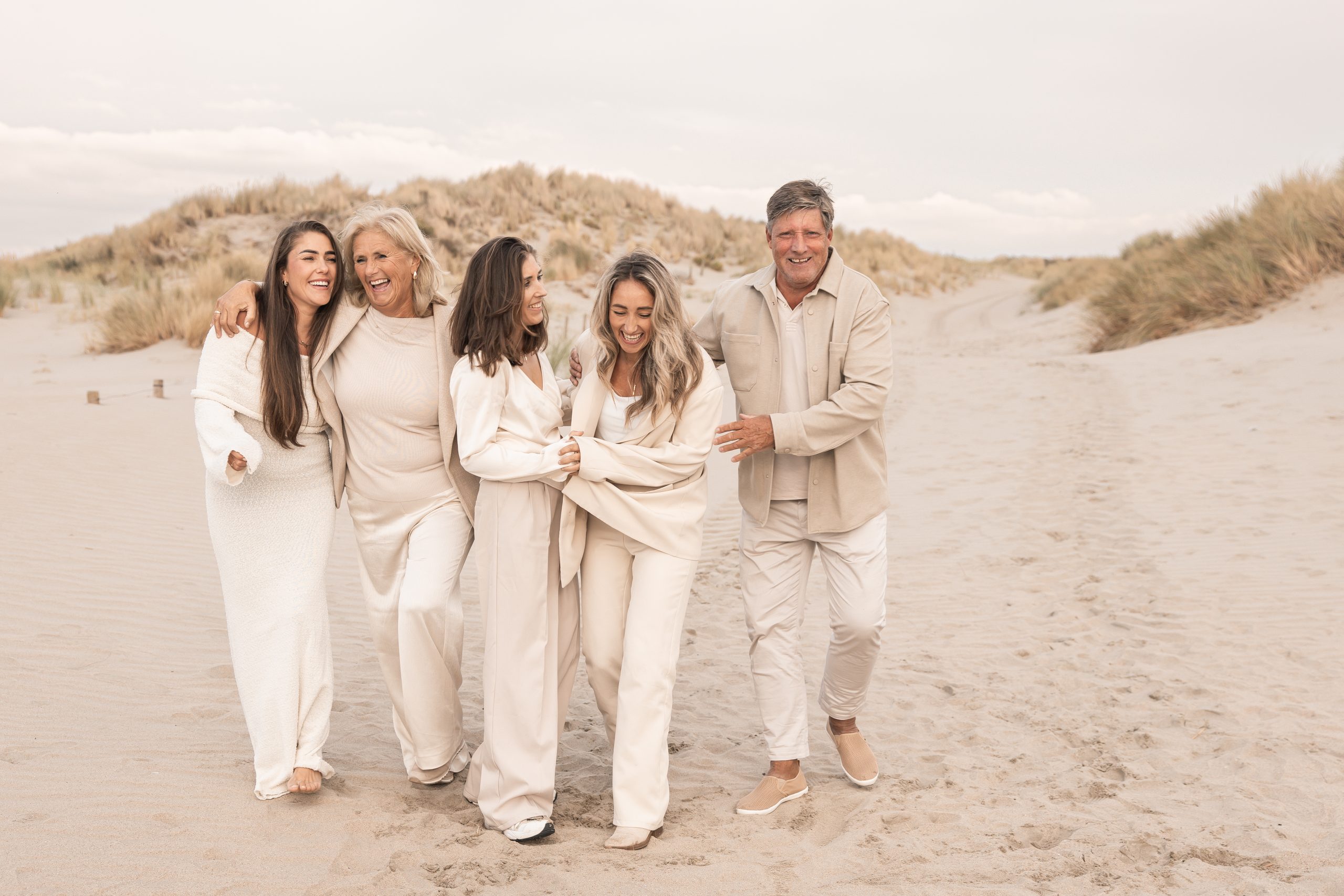 Lifestyle familiefoto op het strand met volwassen kinderen en ouders in zachte beige tinten; liefdevolle en spontane momentopname in de duinen, geportretteerd door By Iris van der Zwan in het Westland, ’s-Gravenzande en regio Den Haag.