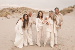 Lifestyle familiefoto op het strand met volwassen kinderen en ouders in zachte beige tinten; liefdevolle en spontane momentopname in de duinen, geportretteerd door By Iris van der Zwan in het Westland, ’s-Gravenzande en regio Den Haag.